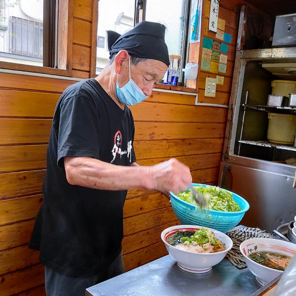 ラーメン調理中。あらかじめ切り分けたチャーシューをスープの大鍋にさっと浸し、温めてから麺にのせる